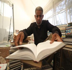 بائع الكتب محمد رمضان سعد يعرض مجموعة من الكتب التي أنقذها من ركام منزله المدمر في بيت لاهيا داخل كشك مؤقت بمدينة دير البلح، بعد تدمير العديد من المكتبات ومتاجر الكتب في قطاع غزة